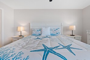 A bedroom with a bed, two bedside tables, a nightstand, a headboard, and a wall-mounted lamp. - Carlos Pointe #222-gulf Haven (Fort Myers Beach)