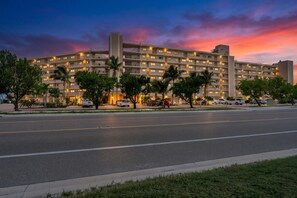 Ein mehrstöckiges Hotel mit schlichter Fassade, vielen Fenstern und einem Parkplatz mit Autos.