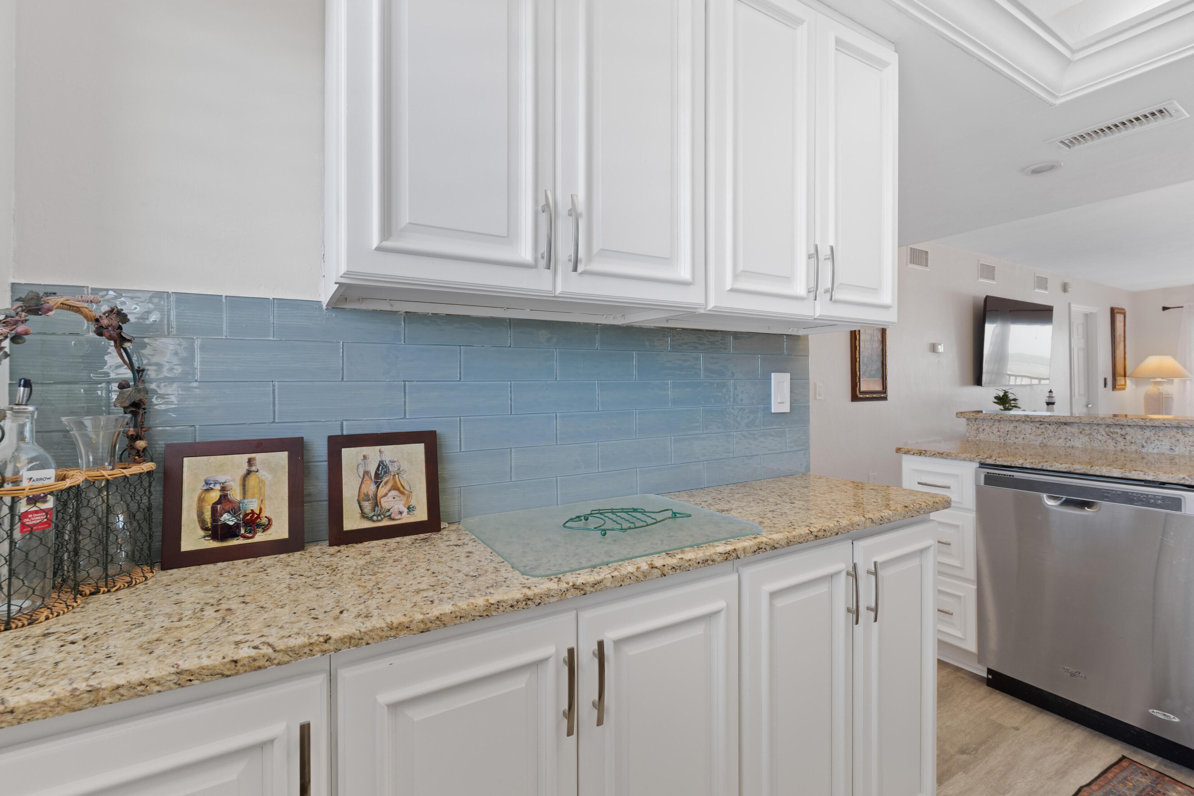 A kitchen with white cabinets, a blue backsplash, a granite countertop, and a dishwasher.