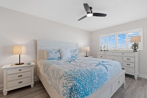 Un dormitorio con cama, mesitas de noche, ventilador de techo y ventana con persianas.