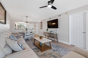 A modern living room with a sofa, coffee table, and dining area. - Carlos Pointe #222-gulf Haven (Fort Myers Beach)