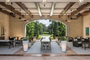 Un espace patio intérieur avec une table et des chaises, entouré de plantes en pot et offrant une vue sur un jardin bien entretenu.