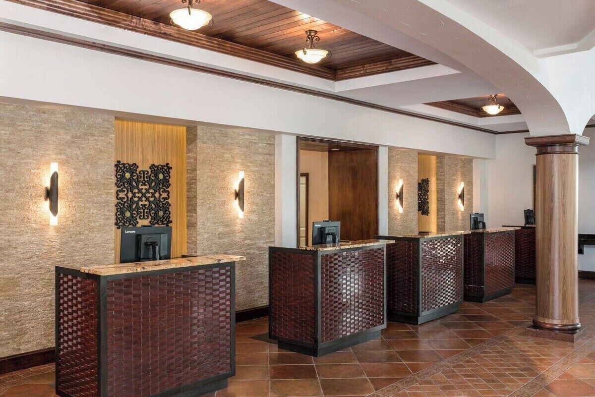 A reception area with a modern design, featuring a reception desk, a wall-mounted decorative panel, and a wooden ceiling.