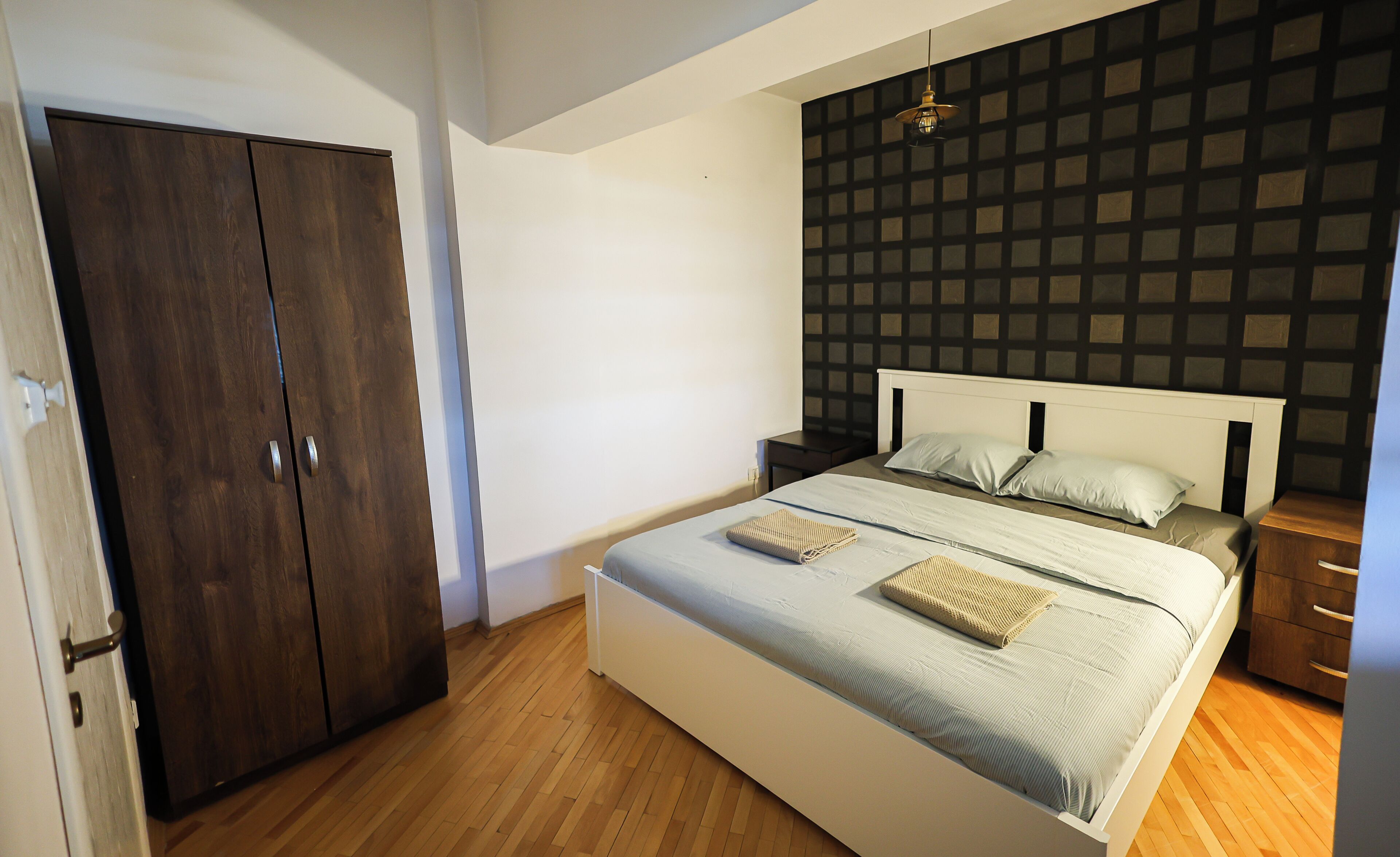 A bedroom with a bed, nightstands, a wardrobe, and a patterned wall.