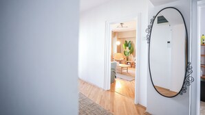 Un couloir avec un miroir, une porte donnant sur une pièce où se trouvent une chaise et une plante, et un plancher en bois.