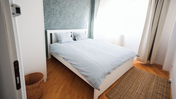 Une chambre à coucher comprenant un lit, une table de chevet, un radiateur fixé au mur et une fenêtre avec des rideaux.