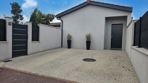 Un bâtiment moderne doté d’un toit plat, d’un portail noir et de deux plantes en pot.