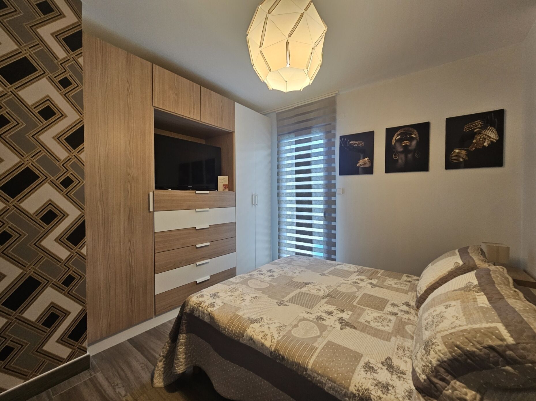 Un dormitorio con cama, armario, televisor y obras de arte en la pared.