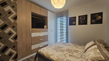 Un dormitorio con cama, armario, televisor y obras de arte en la pared.