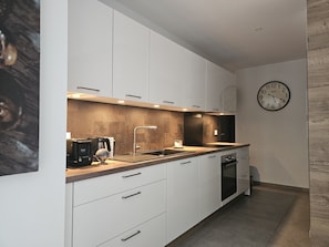 A modern kitchen with white cabinetry, a stainless steel sink, and a clock on the wall.