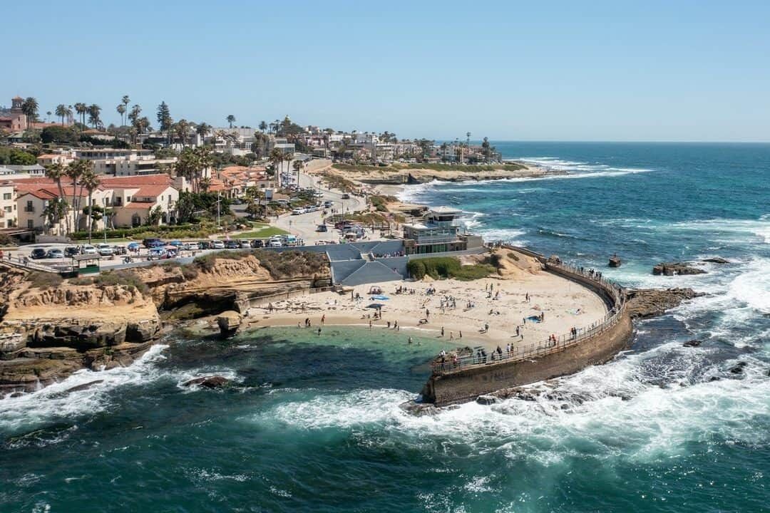 A coastal town with a beach, rocky cliffs, and a pier.