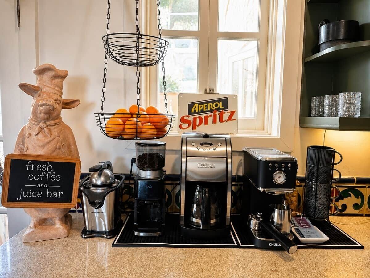 Una estación de café con una cafetera, un molinillo y una cesta de naranjas.