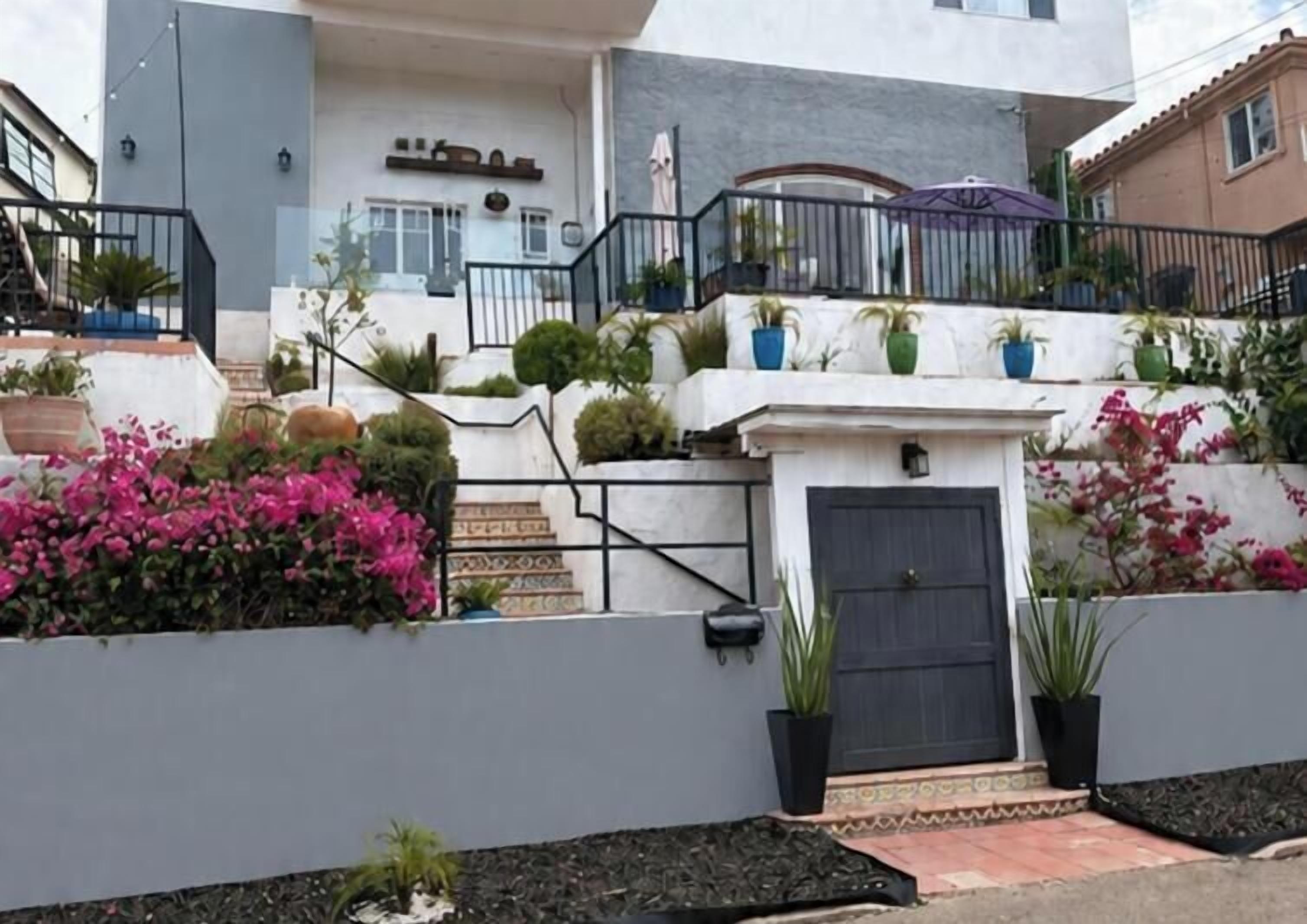 A multi-story building with a staircase leading to a balcony, potted plants, and a door with a small porch area.