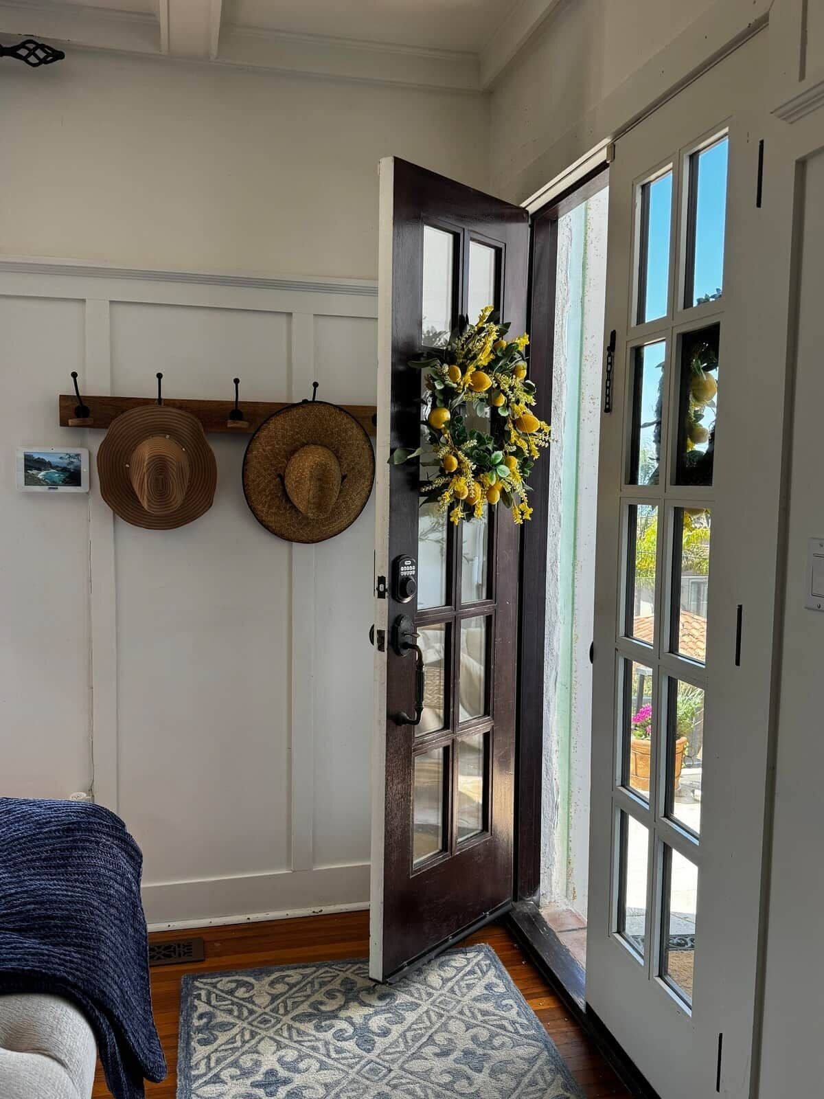 A room with a dark wooden door, a hanging wreath, and two hats on a wall-mounted rack.