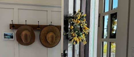 Une pièce avec une porte en bois sombre, une couronne décorative suspendue et deux chapeaux posés sur un porte-chapeaux fixé au mur.