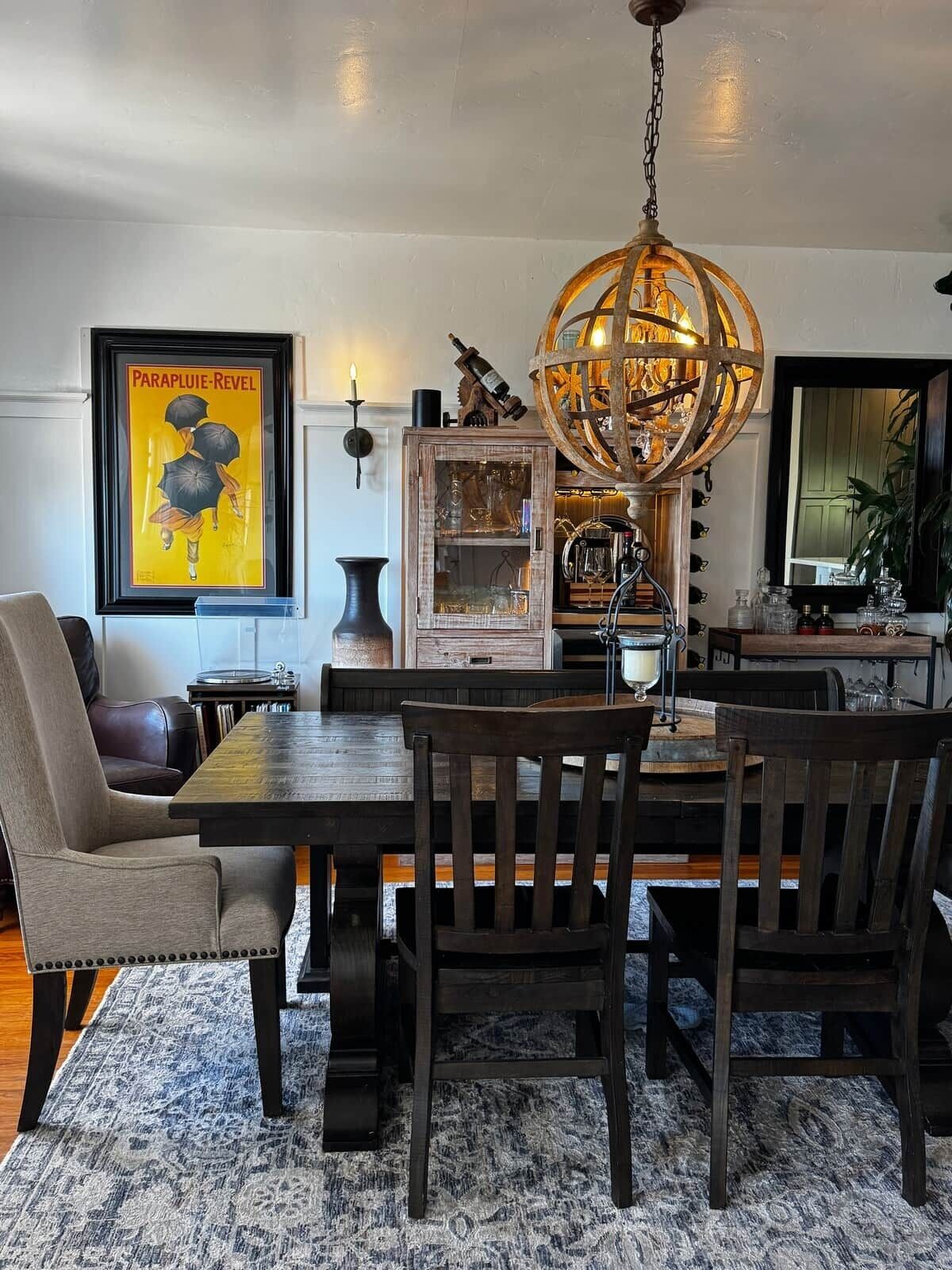 A dining area with a wooden table and chairs, a chandelier, and a framed poster on the wall.