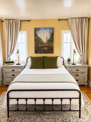 A bedroom with a bed, two nightstands, a painting, and curtains. - Amalfi House/Hot Tub/Pizza Oven/Ocean Views (San Diego)