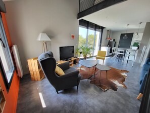 Een moderne woonkamer met een bank, televisie en een eethoek met stoelen en een tafel.