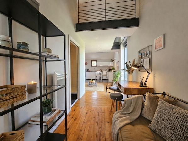Un intérieur moderne avec un plancher en bois, un canapé, un bureau et une cuisine en arrière-plan.