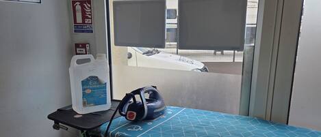 Una habitación con una tabla de planchar azul, un extintor y una ventana con persianas.