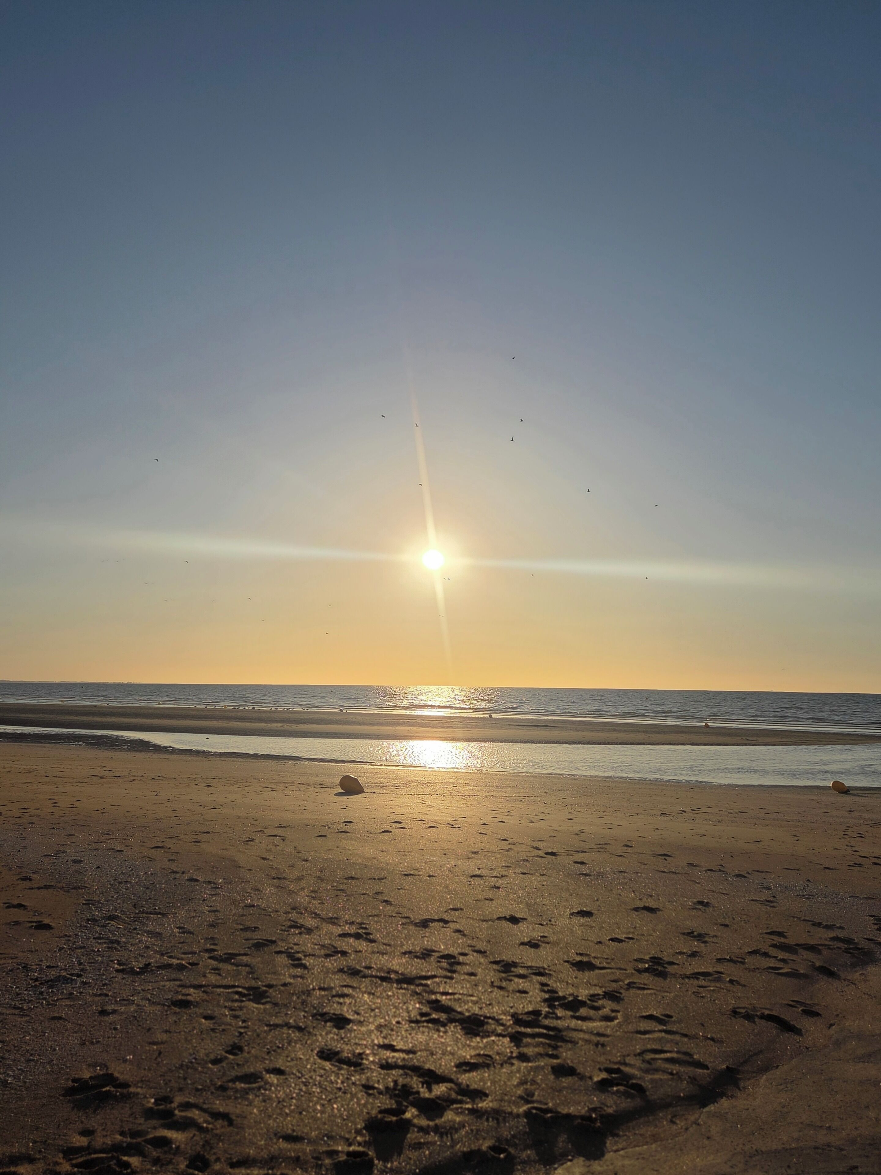 Ein Strand mit Fußabdrücken und der tiefstehende Sonne am Horizont.