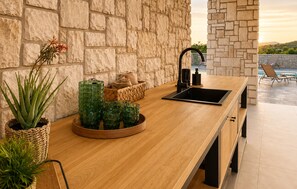 A modern kitchen with a stone wall backdrop, a wooden countertop, and a built-in sink. - Amazing home in Kolan with sauna (Kolan)