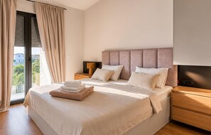 A modern bedroom with a large bed, a flat-screen TV, a wooden nightstand, and a view of the outdoors. - Amazing home in Kolan with sauna (Kolan)