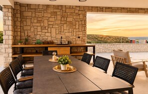 An outdoor dining area with a stone wall backdrop, a long table, and several chairs. - Amazing home in Kolan with sauna (Kolan)