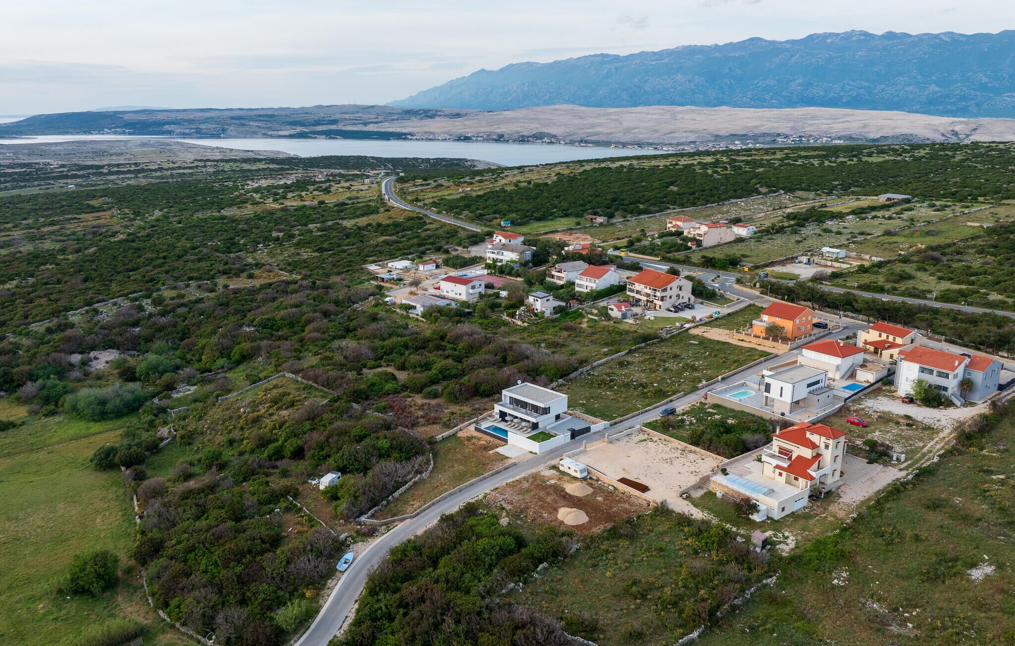 Vista aérea de una zona residencial con casas, una carretera y una masa de agua al fondo.