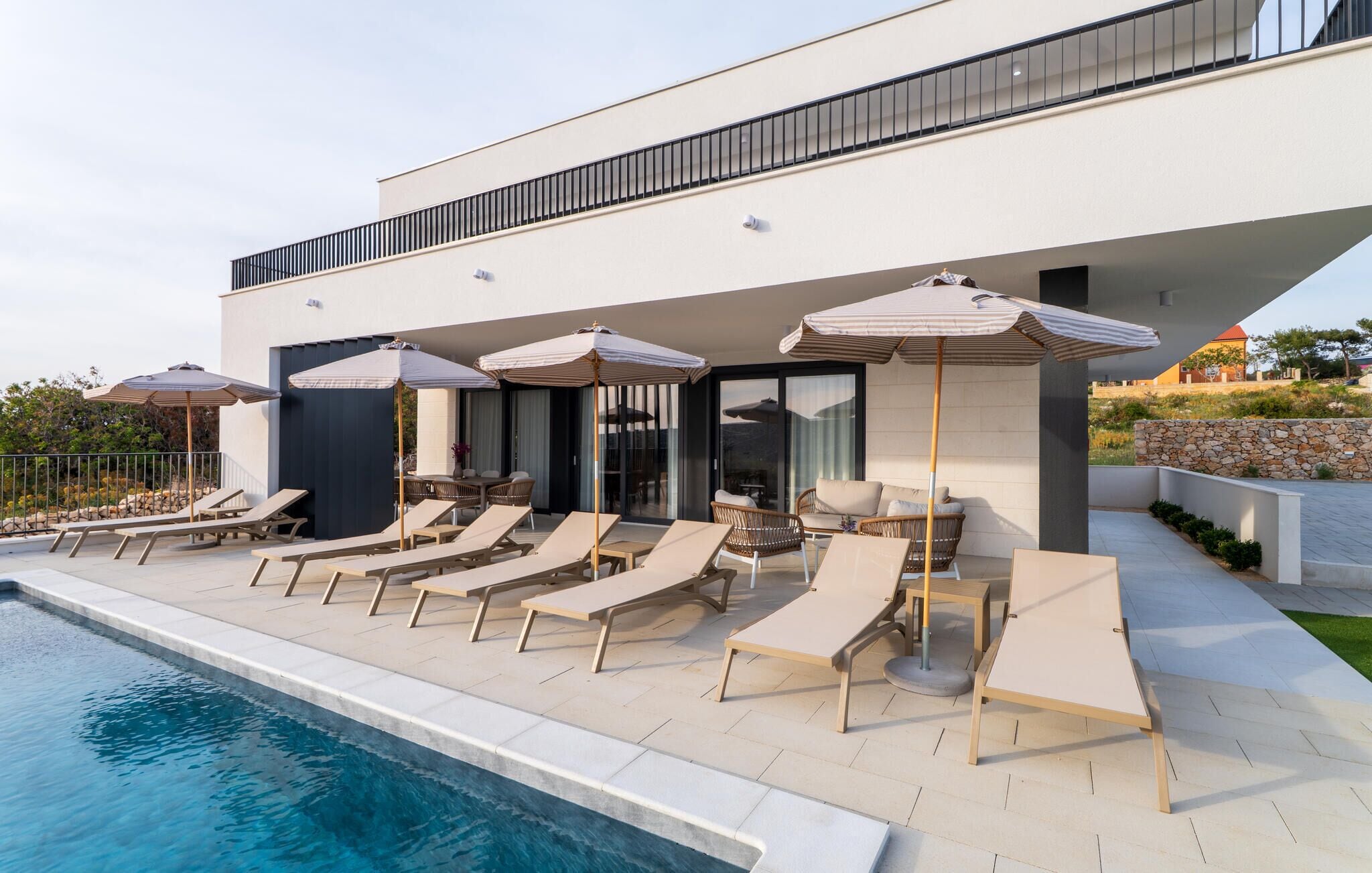 A modern outdoor pool area with lounge chairs and umbrellas, a clear pool, and a building with large windows and a balcony.