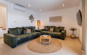 Ein Wohnzimmer mit Ecksofa, rundem Couchtisch, Stehlampe und an der Wand montiertem Fernseher.