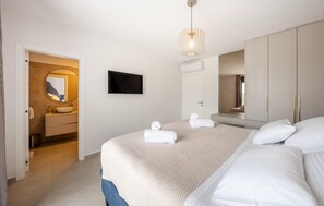 Ein Schlafzimmer mit Bett, Fernseher, Spiegel und einem Badezimmer inklusive Waschbecken und Handtuchhalter.