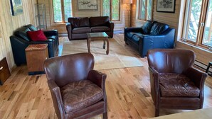 A wooden cabin interior with two sofas, a coffee table, and leather armchairs. - Waterfront Chalet! The Getaway You Need! (Lantier)