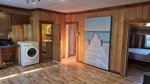A wooden interior with a washing machine, a painting of a pier, and a bed. - Waterfront Chalet! The Getaway You Need! (Lantier)