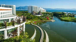A modern hotel with a curved water feature, lush greenery, and a view of the ocean. - The Grand Bliss Nuevo Vallarta Resort 2 bedrooms and AC at Vidanta Resort (Nayarit.)