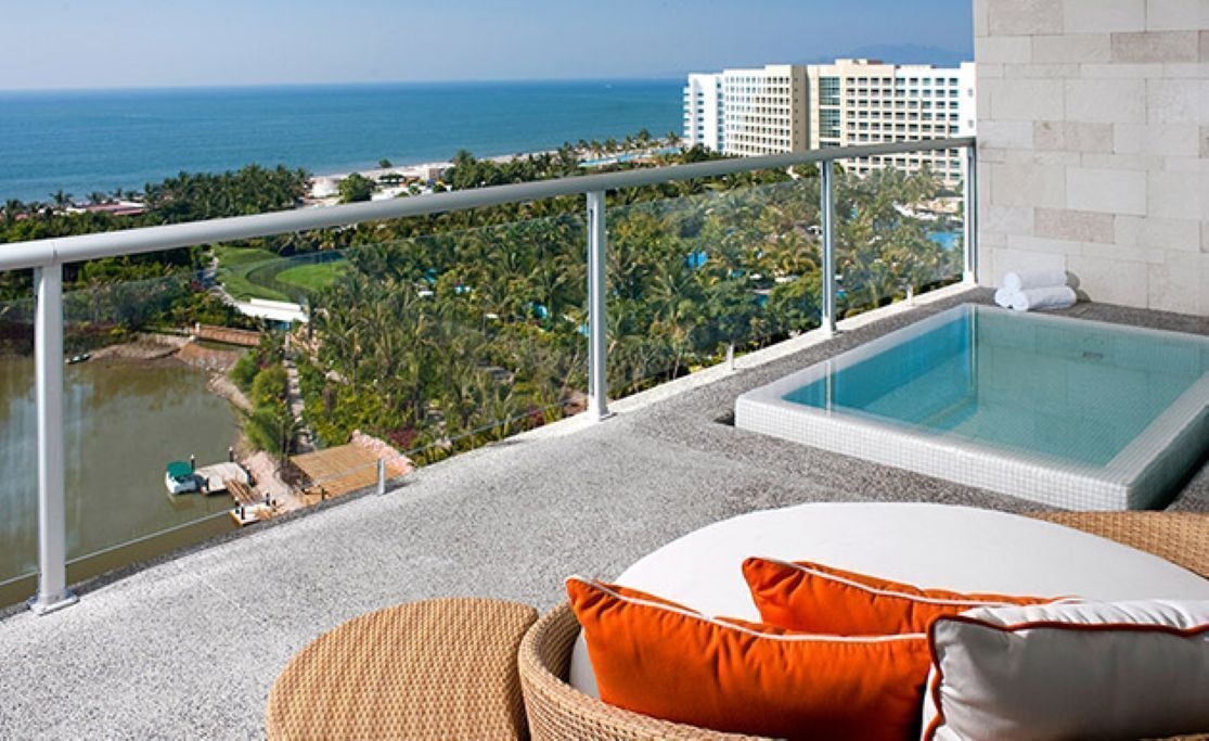 Un balcón con piscina, con vistas a la costa, edificios y vegetación.