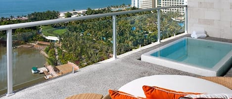 Un balcon avec une piscine, donnant sur une zone côtière avec des bâtiments et de la végétation.
