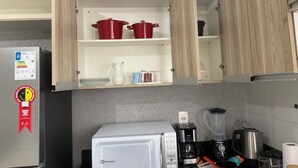 Una cocina con microondas, cafetera, licuadora y un armario con ollas rojas.