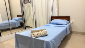 Un dormitorio con cama, espejo y ventana con cortinas.