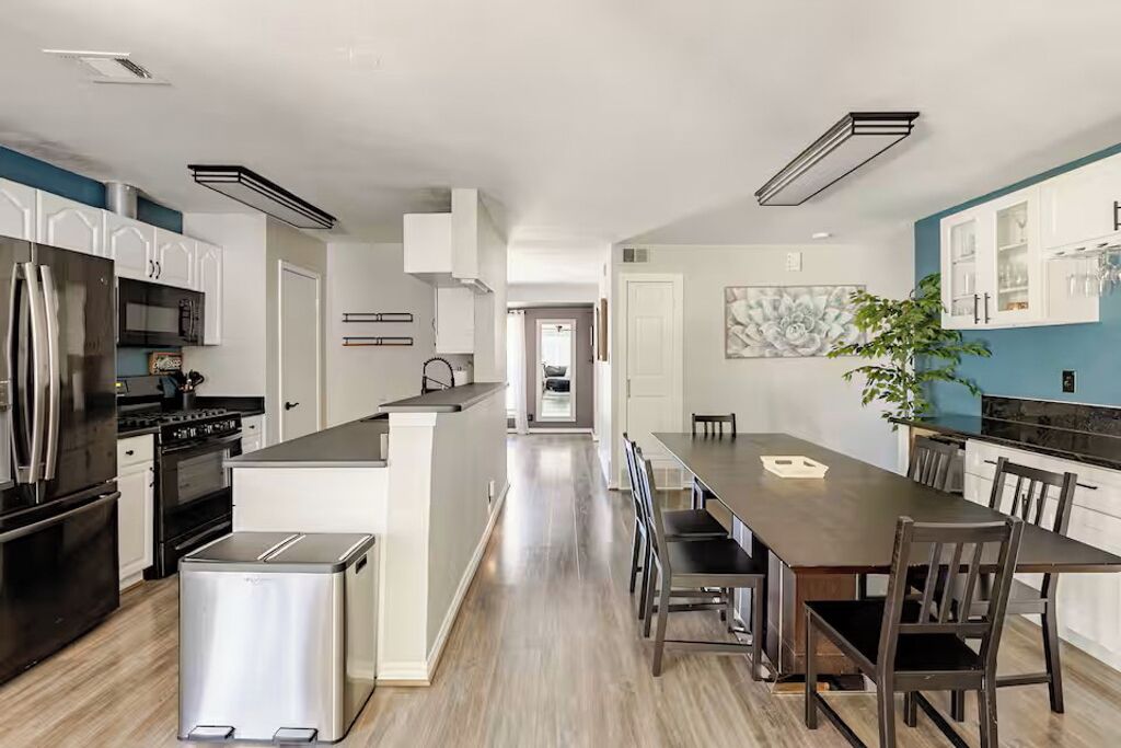 A modern kitchen with stainless steel appliances, a central island, and a dining area with a long table and chairs.