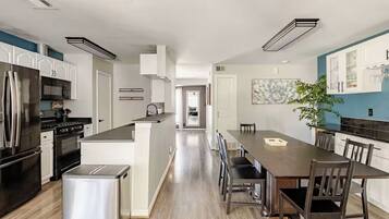 A modern kitchen with stainless steel appliances, a central island, and a dining area with a long table and chairs.
