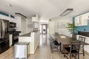 Una cocina moderna con electrodomésticos de acero inoxidable, una isla central y un comedor con una mesa larga y sillas.