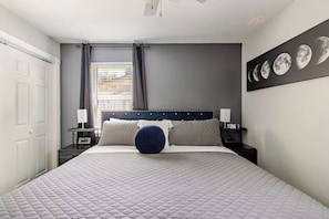 Un dormitorio con cama, mesitas de noche, ventana con cortinas y un panel decorativo con las fases de la luna.