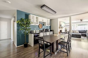 Una cocina moderna con armarios blancos, una mesa de comedor y sillas. Hay una planta en maceta y un cartel que dice 'WHISKEY'.