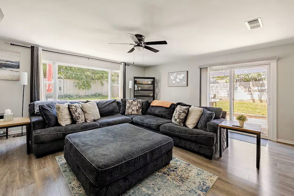 A living room with a sectional sofa, a ceiling fan, and a view of the outdoors.