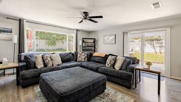 A living room with a sectional sofa, a ceiling fan, and a view of the outdoors.