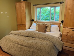 Ein Schlafzimmer mit einem Bett, einem Holzschrank und einem Fenster mit Blick ins Grüne.