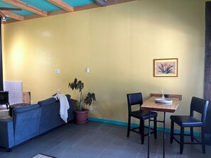 Ein Zimmer mit einer Couch, einem Tisch mit Stühlen, einer Topfpflanze und einem gerahmten Bild an der Wand.