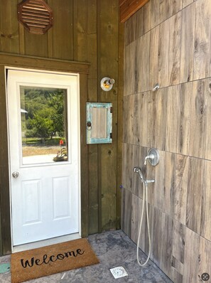 A wooden door with a window, a shower with a hose, and a welcome mat. - Chetco Riverfront Cottage / Hot Tub / Ev Charger (Brookings)