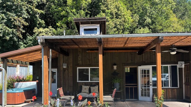 Una casa de madera con porche cubierto, jacuzzi y jardín con diversas plantas y flores.